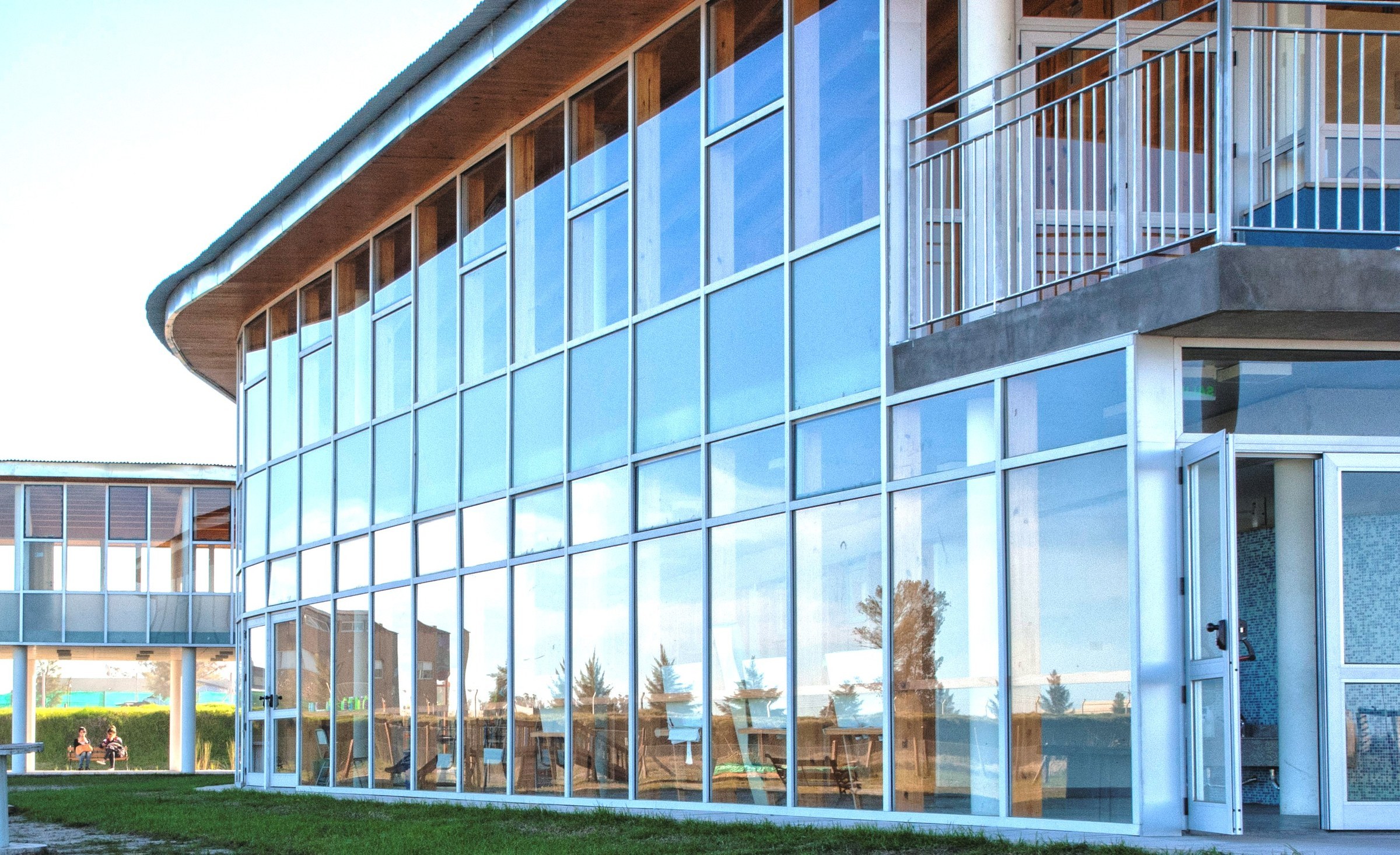 La fachada vidriada de uno de los edificios del colegio de día, con el cielo y el parque reflejados en los vidrios